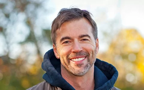 man in the outdoors smiling after practicing techniques for gum recession prevention