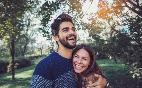 Man and Woman Couple outside in a wooded area laughing and smiling while hugging